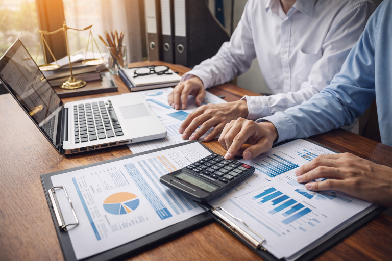 Profissionais de contabilidade empresarial analisando relatórios financeiros, gráficos e cálculos em ambiente corporativo.